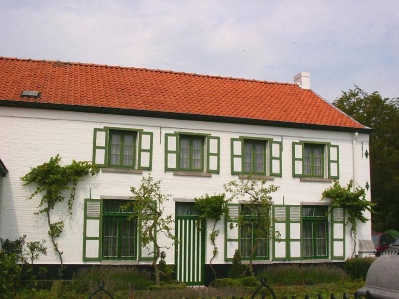Groot wit gebouw met een oranje dak en groene ramen. Vandaag het Damiaanmuseum in Ninde.