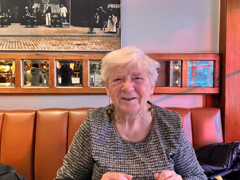 Foto van Lieve Van der Velden in een cafeetje in Antwerpen. Op de achtergrond een rij kleine spiegeltjes met daarboven een oude zwart-witfoto
